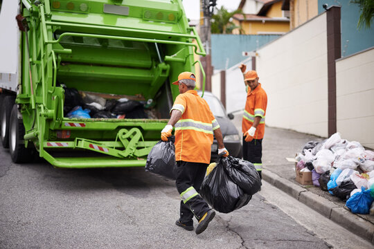 Two sanitation workers loading black trash bags into a green garbage truck on a residential street — garbage removal services Kent WA.