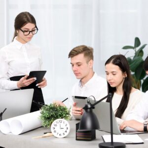 A group of business professionals working together at a desk, using laptops, tablets, and documents during a team meeting in an office.