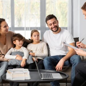 Family sitting together on a sofa during a counselling session, speaking with a therapist in a comfortable home setting.